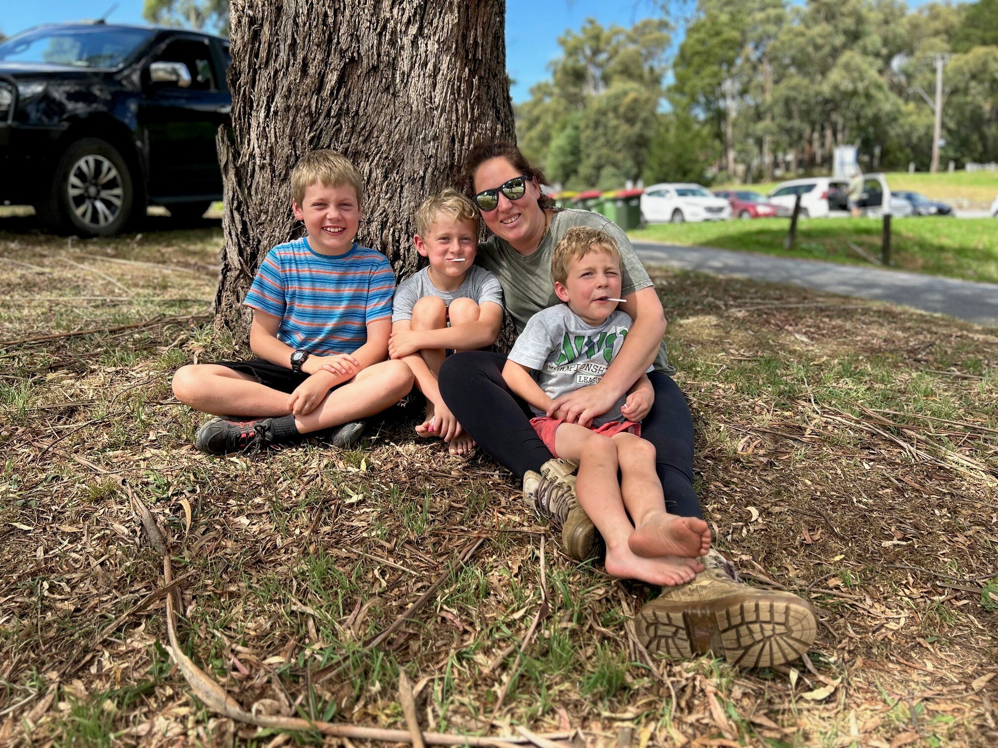 A woman and three young boys sit under a tree.