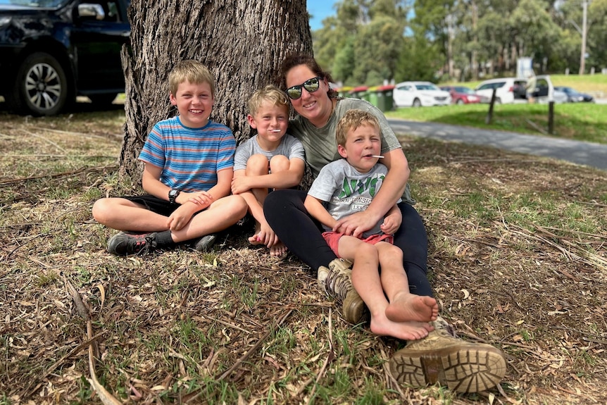 A woman and three young boys sit under a tree.