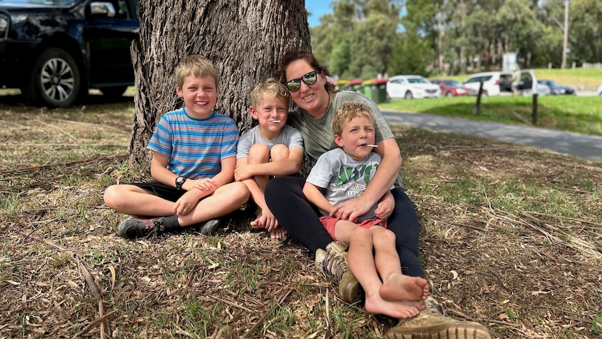 A woman and three young boys sit under a tree.