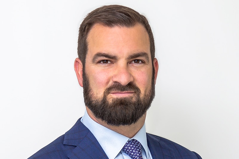 Headshot of man with beard wearing suit and tie