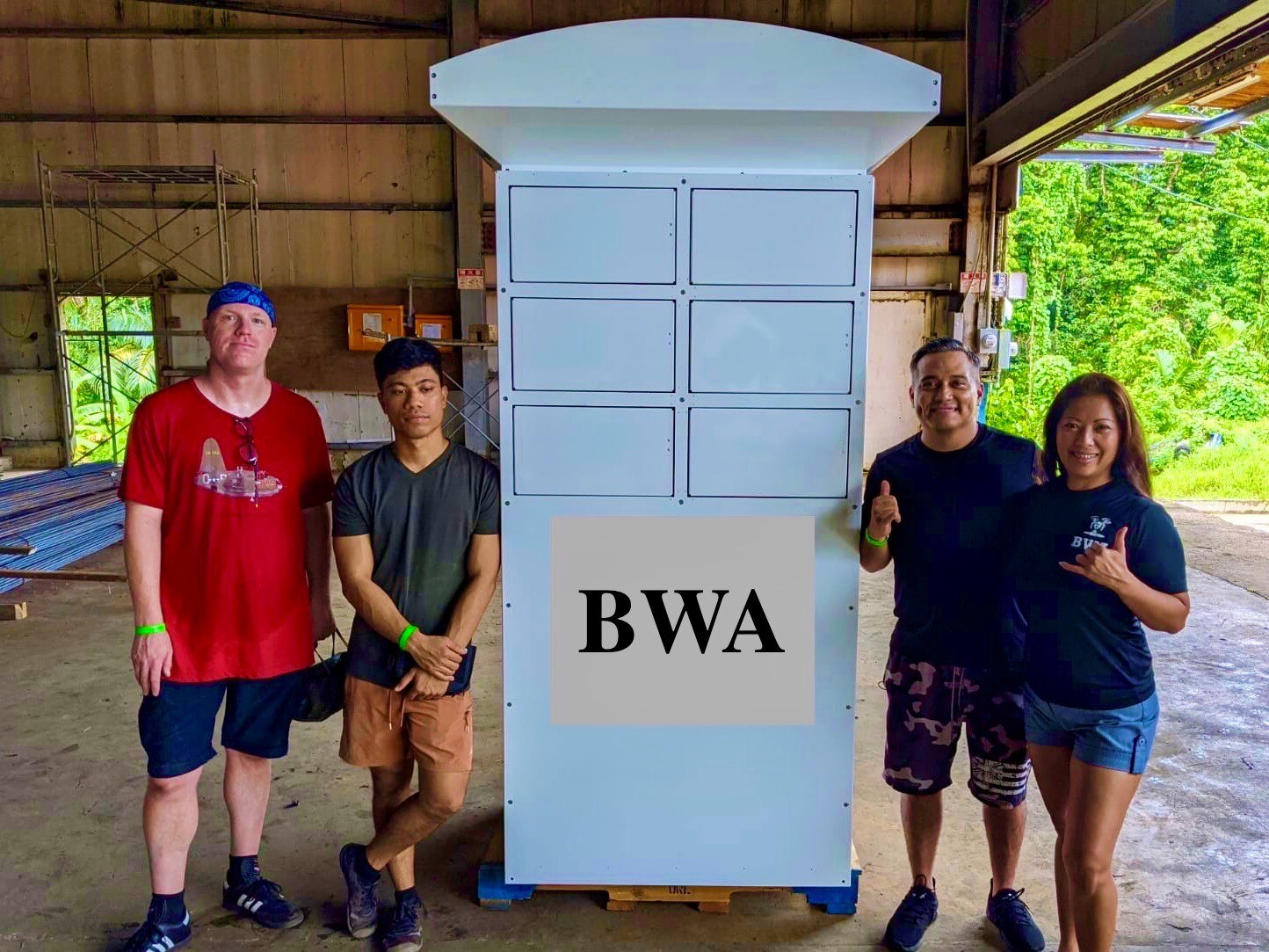 Four people stand beside a large metal container with the words MWA printed on the front