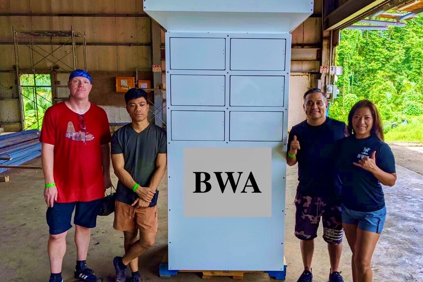 Four people stand beside a large metal container with the words MWA printed on the front