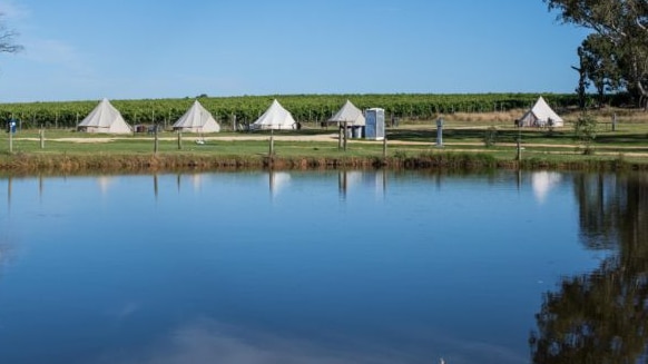 Lake in foreground with glamping tents and vineyard in background