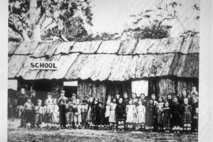 Black and white photograph of more than 20 students standing in of timber school building.