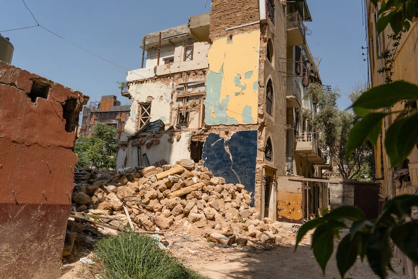 A pile of rubble sits beside a street lined with buildings.