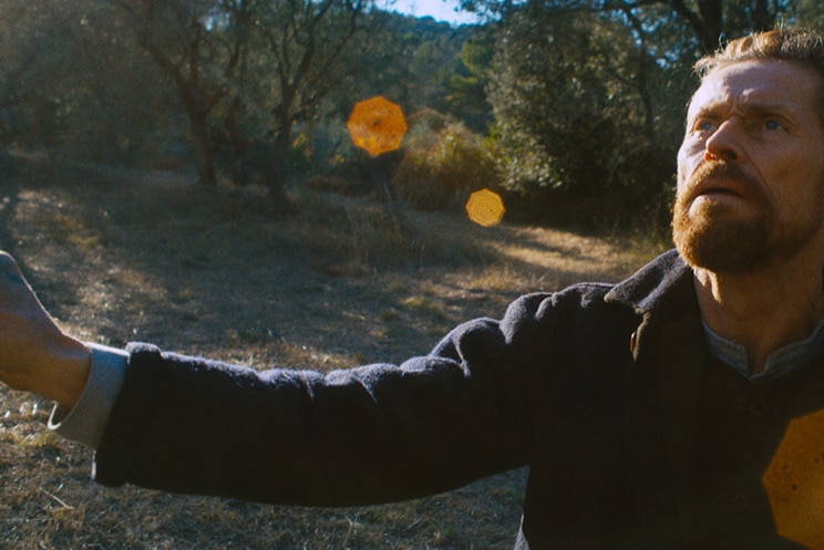 Colour still of Willem Dafoe looking up and painting in the countryside in 2018 film At Eternity's Gate.