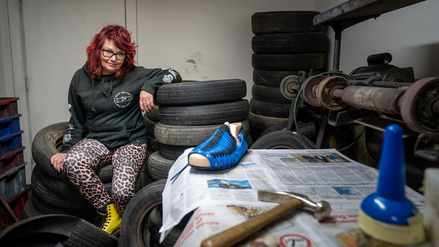 A woman sits on a pile of tyres with cobbler tools nearby.