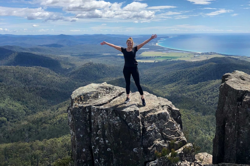 A woman on a rock up high with coastline in the background