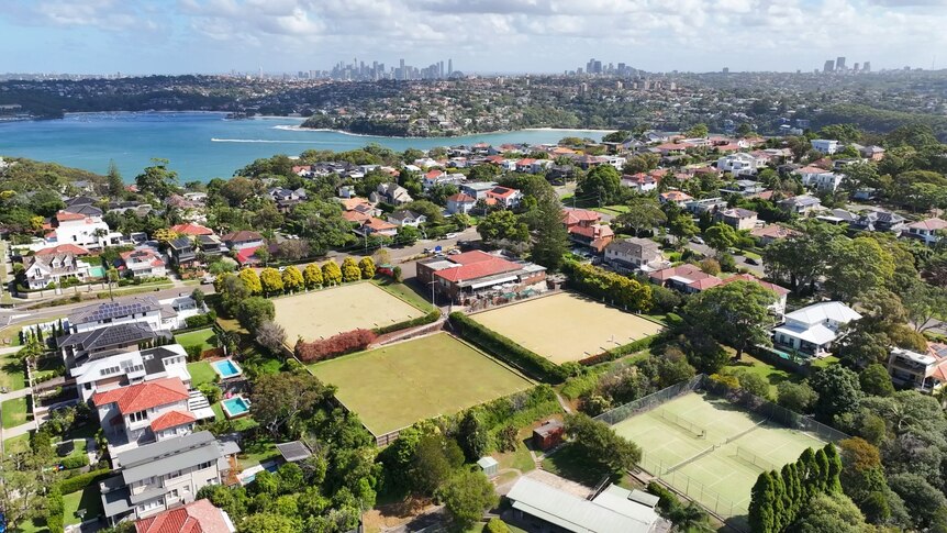 An aerial shot of the Balgowlah Bowling Club with the city in the background and a blue waterway in the middle ground. 