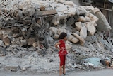 Girl stands by building damaged by Syrian forces