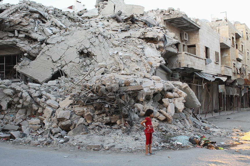 Girl stands by building damaged by Syrian forces