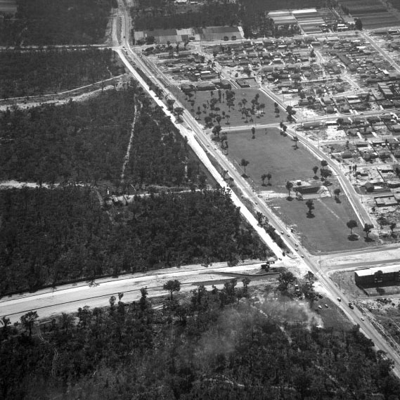 Black and white aerial photo of road, bushland and housing