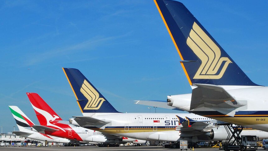 Against a blue sky, the tails of four Airbus A380 aircraft are shown descending diagonally down a runway.