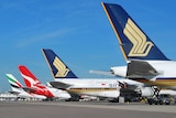 Against a blue sky, the tails of four Airbus A380 aircraft are shown descending diagonally down a runway.