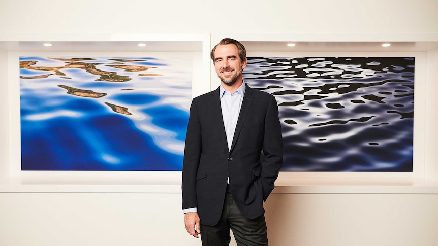 Prince Nikolaos standing in front of photographs he took of the ocean and Greek islands.