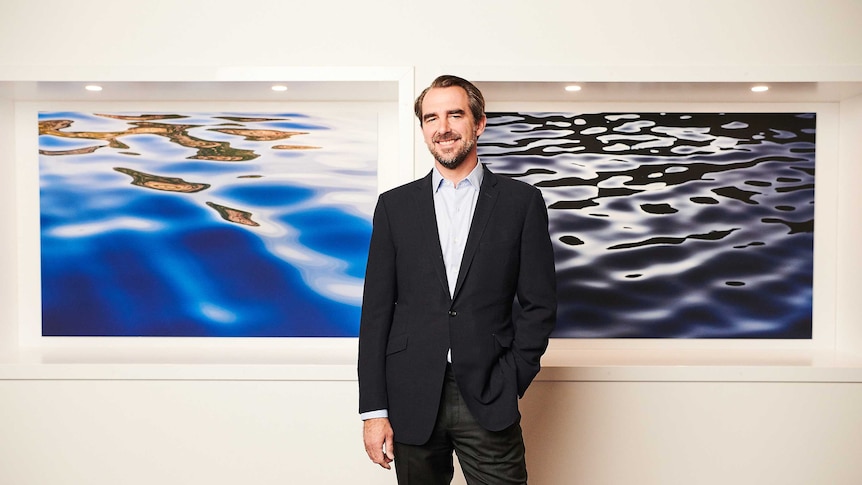 Prince Nikolaos standing in front of photographs he took of the ocean and islands.