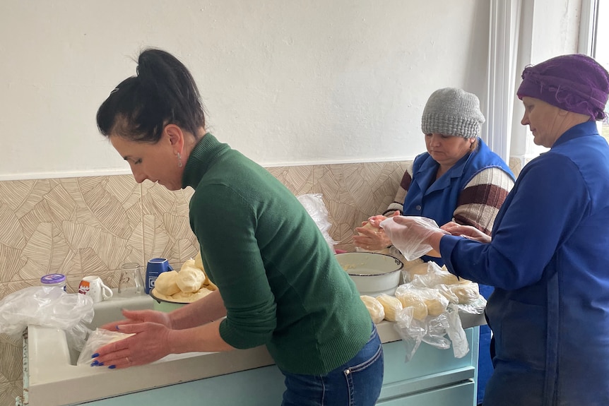 three women surround a bench, packing handfuls of cheese into plastic bags