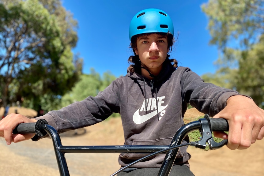A teenage boy wearing a helmet while holding the handlebars of a bike