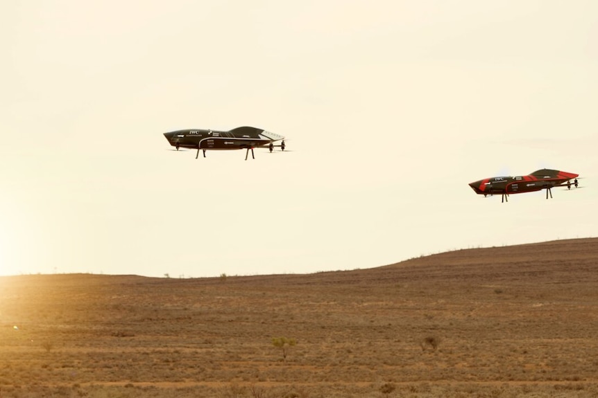 Two flying objects that look like drones suspended in the sky above a desert background.