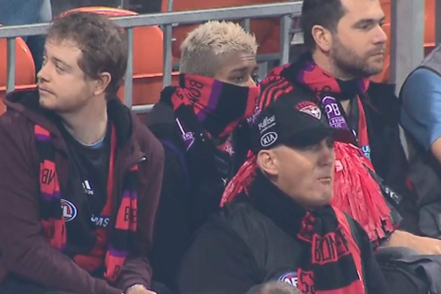 Essendon fans in using their scarves to cover their mouths.