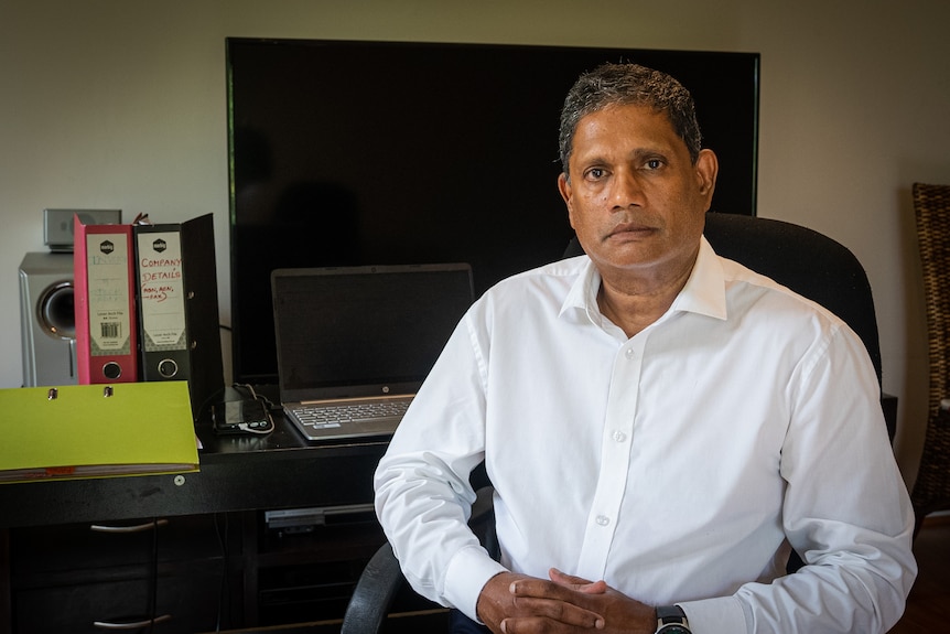 A man in a long-sleeved white shirt sits in his home office.