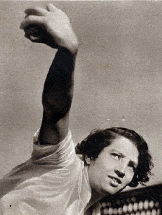 A black and white image of Peggy Antonio rolling her arm over with a ball in her hand.