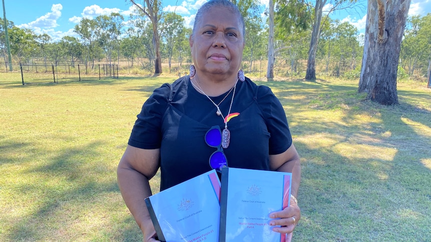 An Indigenous woman stands outside holding native title documents.