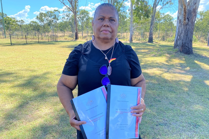 An Indigenous woman stands outside holding native title documents.