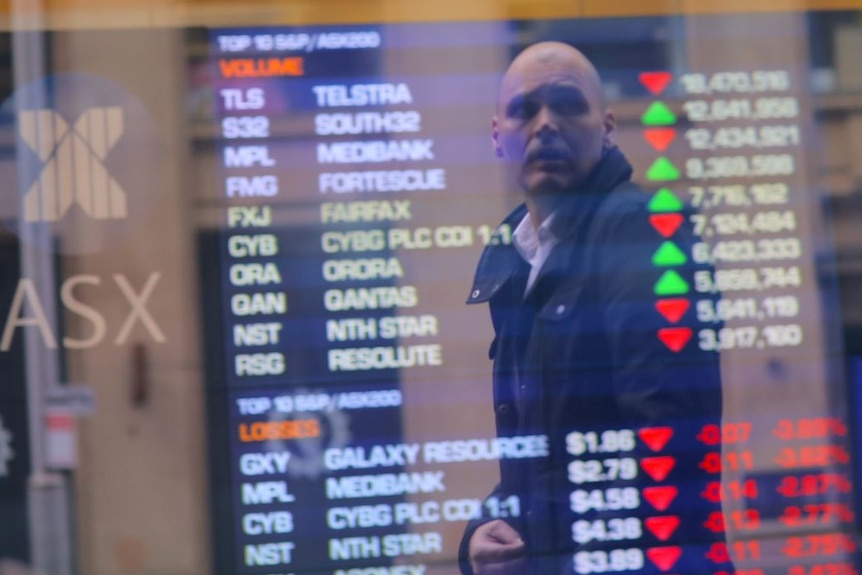 An investor is reflected in a window displaying a board showing stock prices at ASX.