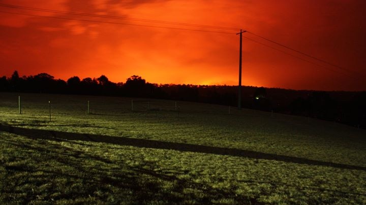 A glowing orange sky hangs over a green paddock, lit by bright spotlights.