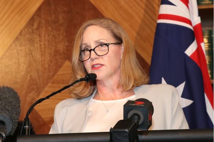 Le PDG d'Austrac, Nicole Rose, s'exprimant lors d'un pupitre de conférence de presse devant un drapeau australien
