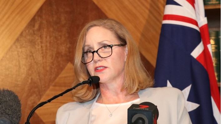 Austrac CEO Nicole Rose speaking at a press conference lectern in front of an Australian flag