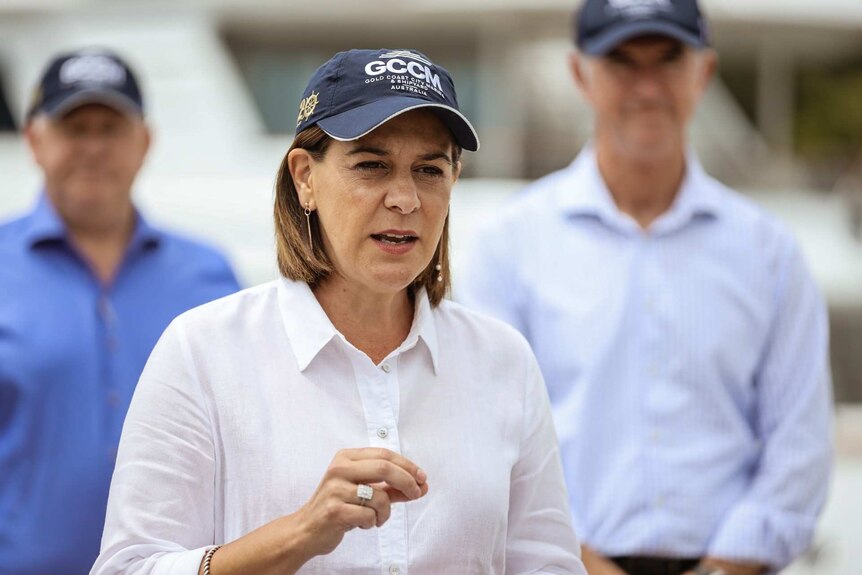 A woman in a white shirt talks while wearing a cap.