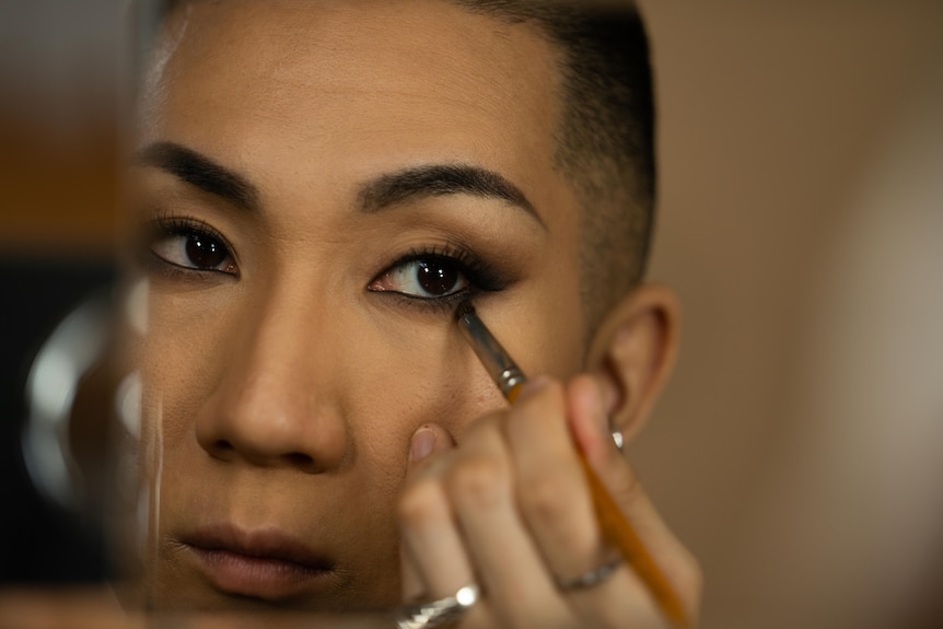 A Japanese man with a buzz cut brushes dark shadow under his eye