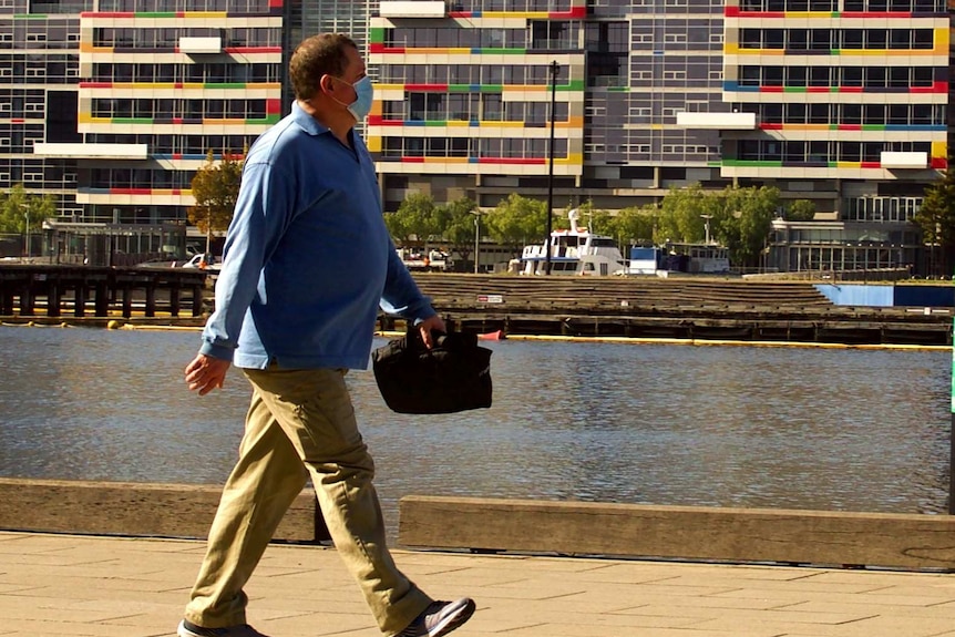 A man walks near the water on a sunny day in Docklands.