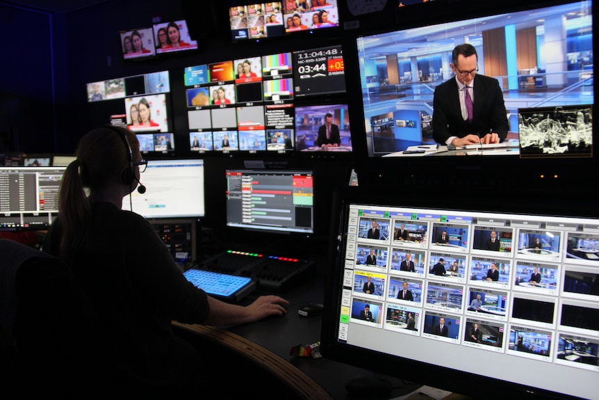 Interior of TV studio with a woman wearing a headset looking at a bank of dozens of TV monitors.