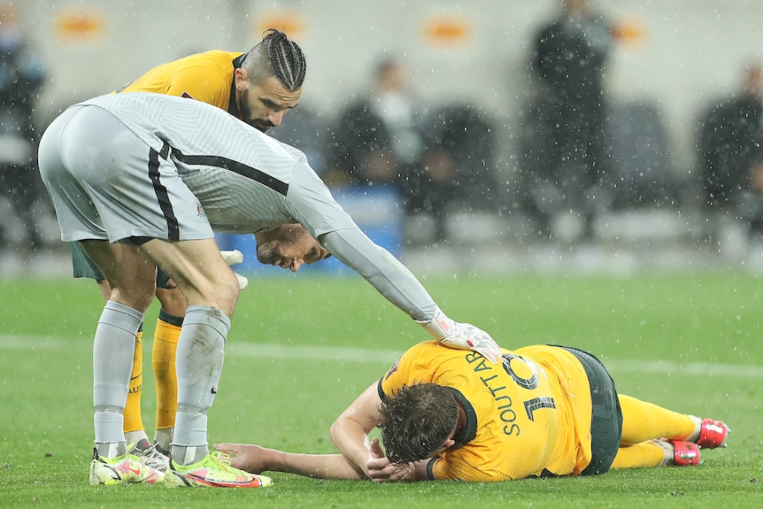 Harry Souttar lies on the ground as Mat Ryan bends over and puts his hand on him