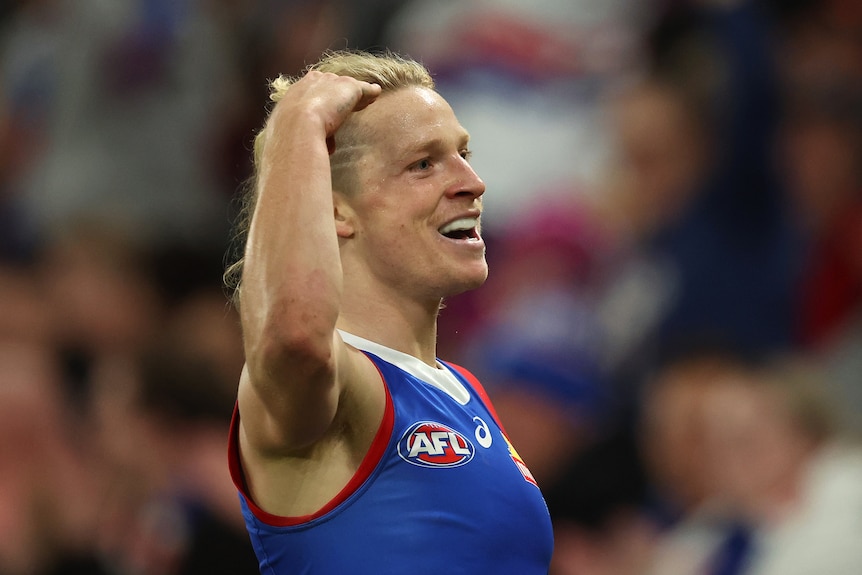 AFL player Cody Weightman celebrates, holding his hand to his head, after kicking a goal.