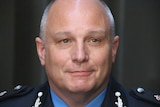 A headshot of Tony Hassall with close cropped grey hair, wearing a prison guard uniform.