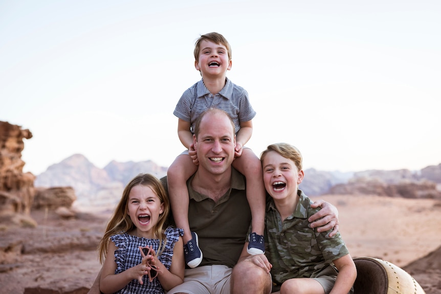prince william smiles with daughter charlotte sitting on his left son george on right and son louis sitting on his shoulders