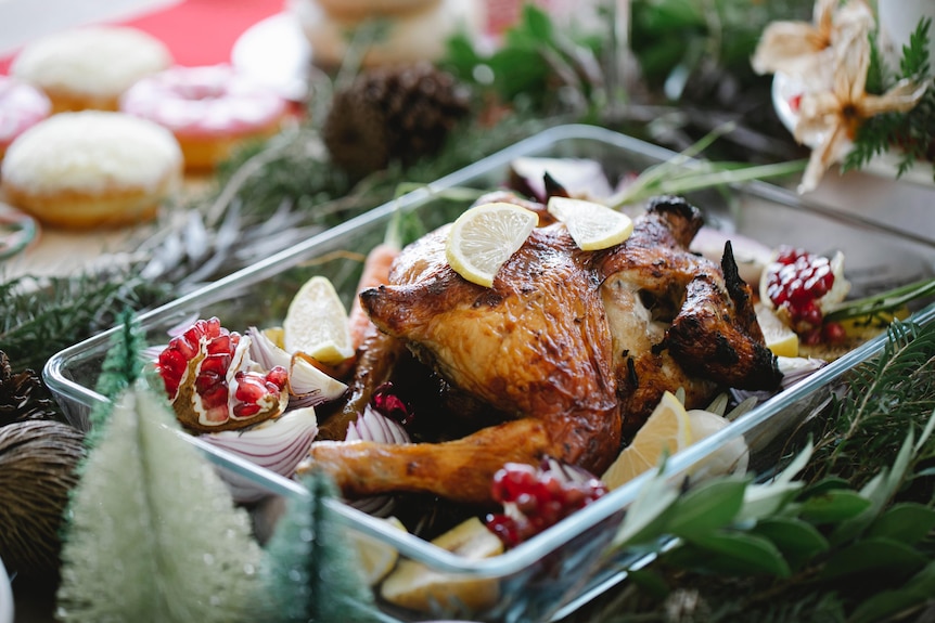Roast turkey in a dish with lemon wedges on top sitting on Christmas table