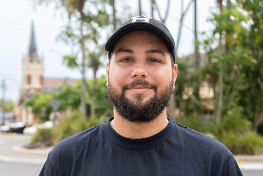 A man with a black beard and cap smiles and looks directly ahead