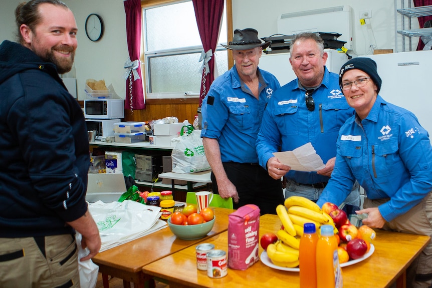 Four people in blue Disaster Relief Australia uniforms sort food on a kitchen table .