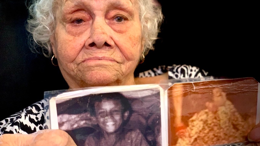 An elderly lady holds up two faded photos of a small, smiling boy.