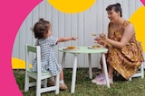 A toddler sits at an outdoor kids table while her mum tries to feed her dinner, the challenges of getting toddlers to eat.