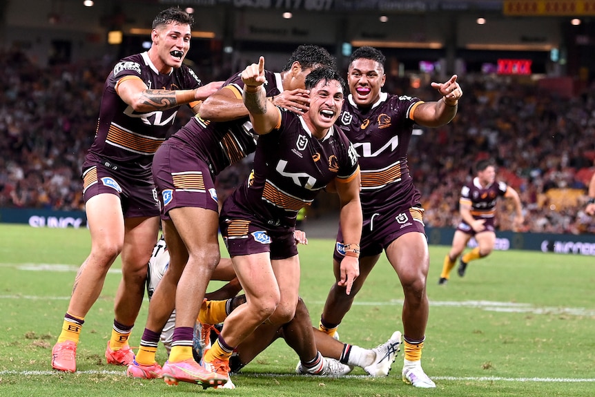 Kotoni Staggs is surrounded by celebrating Brisbane Broncos teammates after a try.