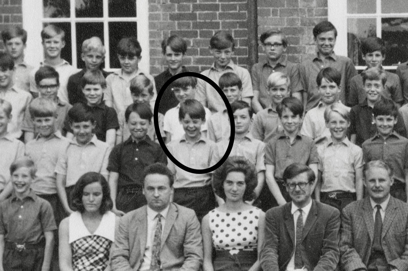 A young boy with brown hair laughs, surrounded by other young boys in a school photo.