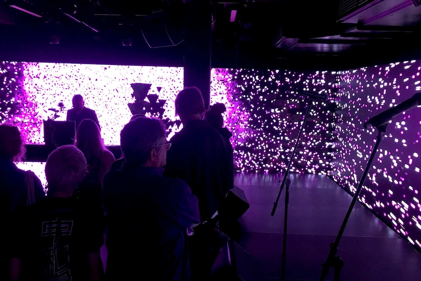 An explosion of light splatters a LED wall around a DJ and onlookers