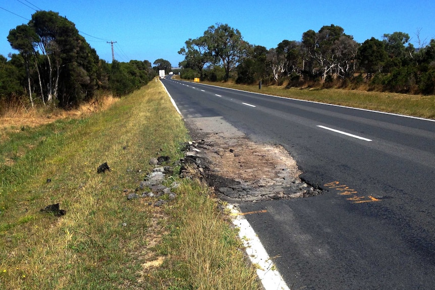 A huge pothole eating into the side of a country highway.