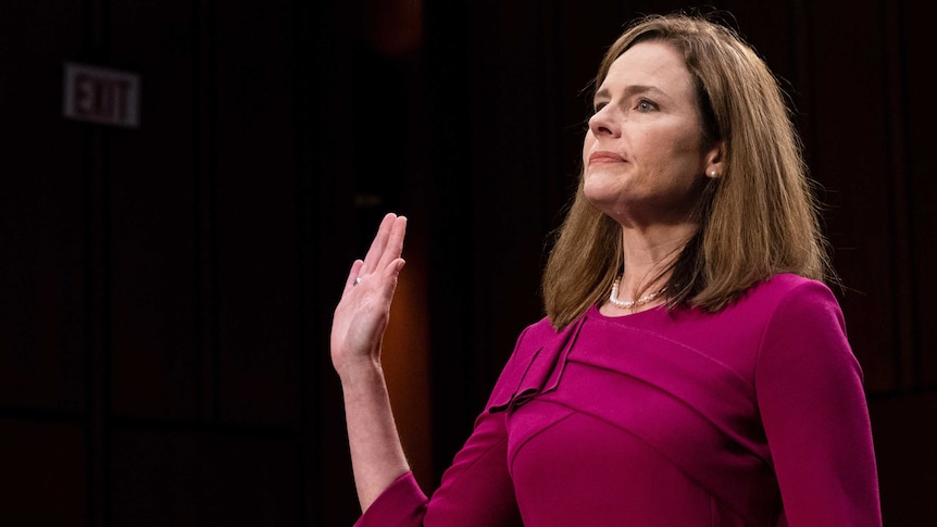 A woman raises her right palm and looks ahead as she stands to swear an oath of office.